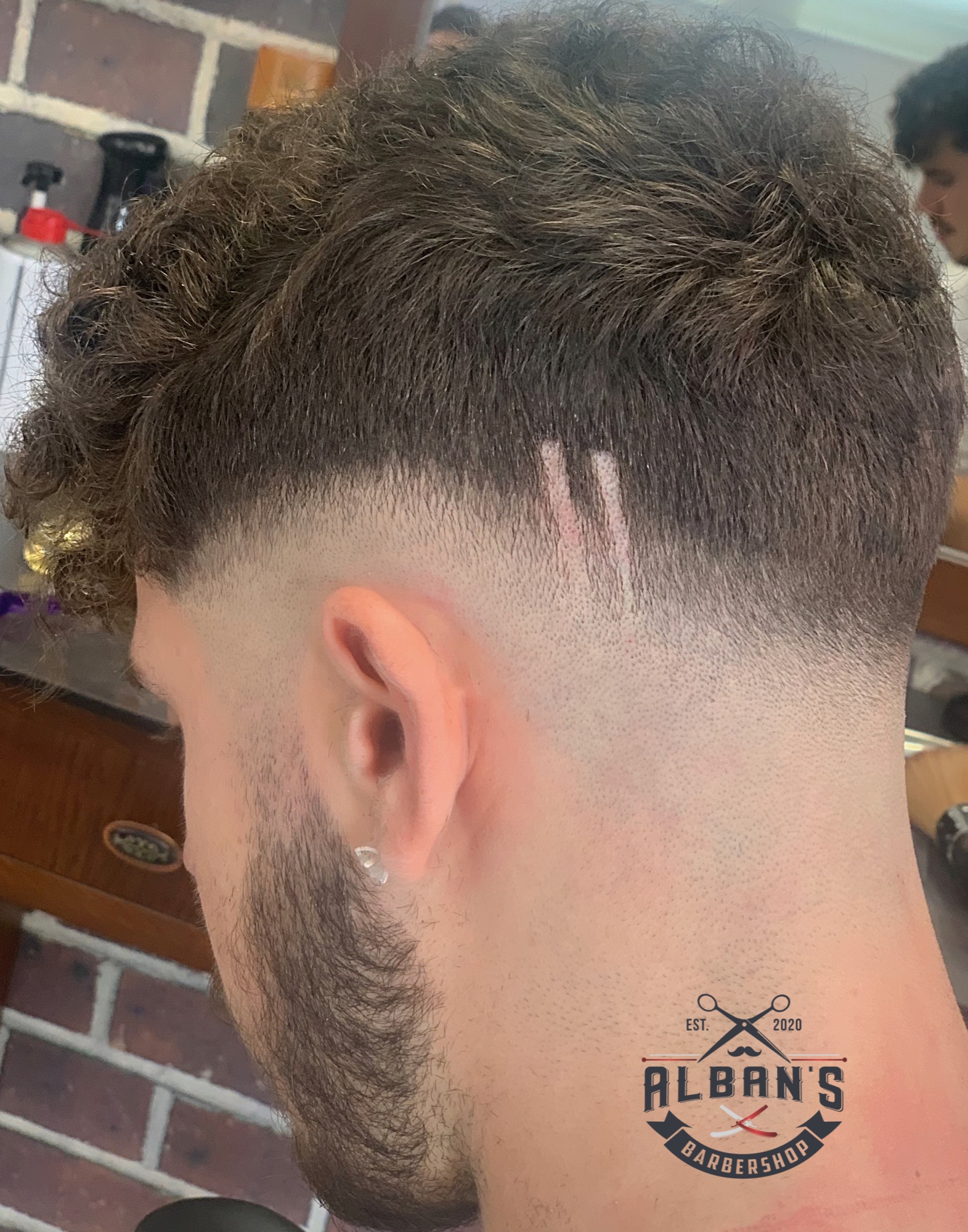 Fade mit Linien am Hinterkopf, mit dem Logo von Alban's Barbershop